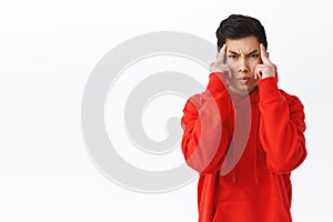 Waist-up portrait of funny asian man trying to use telepathy, read minds or move objects with power of mind, frowning