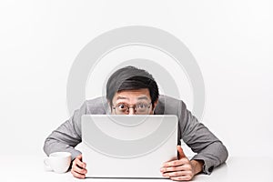 Waist-up portrait of funny and silly handsome asian office worker, man in suit sitting at table hiding face behind