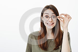 Waist-up portrait of good-looking funny woman in stylish glasses, holding rim with fingers and smiling with strange
