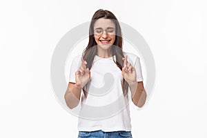 Waist-up portrait of hopeful, excited and optimistic young woman in glasses, cross fingers good luck and close eyes