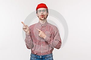 Waist-up portrait impressed and intrigued young caucasian bearded man in glasses, red beanie, pointing upper left corner
