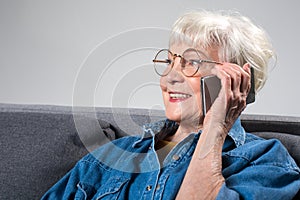 Retired delightful lady talking on phone while sitting on couch