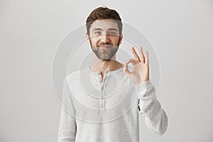 Waist-up portrait of pleased cheerful young man smiling and showing okay or fine gesture in approval or agreement