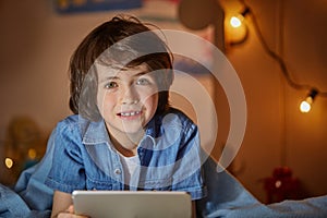 Joyous positive boy with tablet in nursery photo