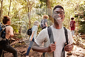Waist up portrait of smiling millennial African American man hiking in a forest with friends, close up