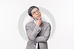 Waist-up portrait of thoughtful, creative and smart asian young man in grey suit, office manager, businessman planning