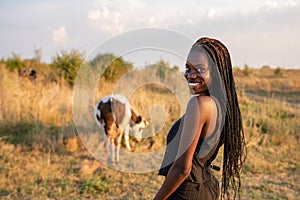 Waist up portrait of the toung african girl in black clothes stands among the field and looking at the camera over her