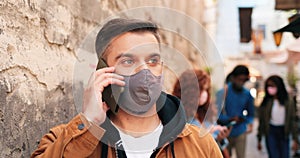 Waist up portrait view of the brunette caucasian man wearing protective face mask having conversation via smartphone on