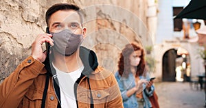 Waist up portrait view of the brunette caucasian man wearing protective face mask having conversation via smartphone on