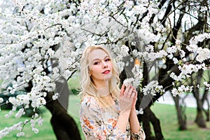 Waist up portrait of young smiling woman with blond hair near blossoming plum tree