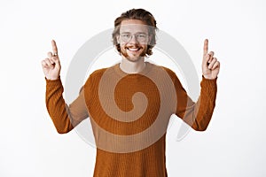 Waist-up shot of charismatic pleased and upbeat handsome young bearded man in glasses with wavy hair, wearing sweater