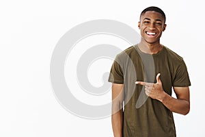 Waist-up shot of cheerful nice and handsome young african american man pointing left with index finger smiling and