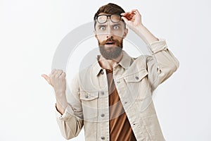 Waist-up shot of concerned questioned handsome mature male with beard taking off glasses staring shocked and stunned at