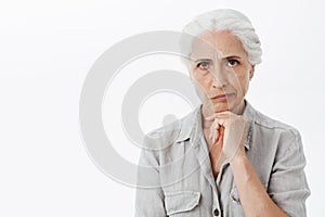 Waist-up shot of concerned serious-looking perplexed elderly woman with grey hair frowning and smirking from