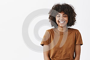 Waist-up shot of cute carefree friendly-looking African American teenage girl with afro hairstyle smiling broadly with