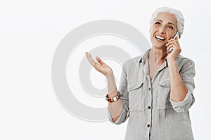 Waist-up shot of delighted caefree kind grandmother talking on telephone and gesturing while being excited and carried