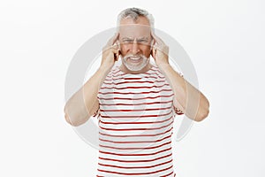 Waist-up shot of disturbed old man with white hair feeling discomfort or painful feeling in head touching temples