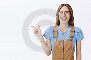 Waist-up shot of enthusiastic charming and charismatic happy girlfriend in brown overalls and transparent glasses