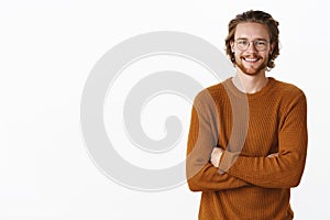 Waist-up shot of friendly-looking delighted european male with long hair and beard in glasses and sweater, holding hands