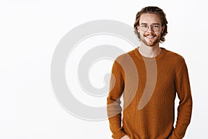Waist-up shot of handsome charming bearded man in glasses with long wavy hair in sweater smiling joyfully at camera as