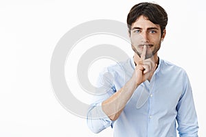 Waist-up shot of handsome successful man with beard and blue eyes smiling naughty making shush gesture over folded