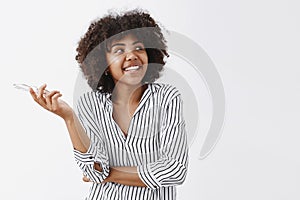 Waist-up shot of happy and carefree modern African American businesswoman in trendy striped blouse holding glasses in