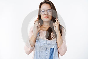 Waist-up shot of hopeful happy and optimistic cute female in glasses squinting and wrinkling nose as eager to wish come