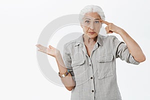 Waist-up shot of irritated smart elderly woman being with son making stupid mistake rolling finger near temple