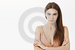 Waist-up shot of offended gloomy and upset cute young female brunette sulking making insulted look crossing arms against