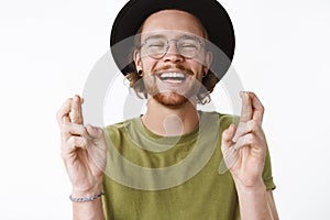 Waist-up shot of optimistic carefree and handsome young bearded guy in glasses and hat laughing out loud with joyful