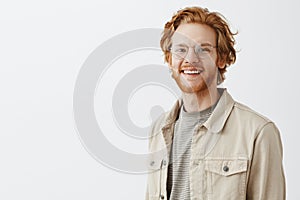 Waist-up shot of pleasant handsome redhead mature guy with beard in transparent glasses and beige jacket over t-shirt