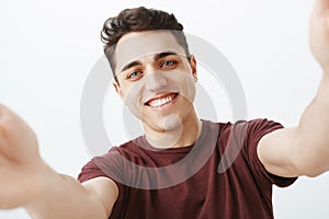 Waist-up shot of pleased happy young european man in trendy red t-shirt, holding camera with hands and making selfie