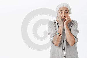 Waist-up shot of scared and concerned old lonely lady feeling unsafe and trembling from fear holding palms near mouth