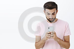 Waist-up shot of shocked and impressed stunned bearded man widen eyes as holding smartphone and looking at mobile phone