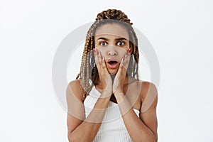 Waist-up shot of shocked and impressed stunned stylish dark-skinned woman with dreads opening mouth from empathy and