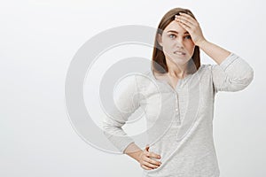 Waist-up shot of smart creative female coworker in white blouse holding hand on forehead biting lower lip being