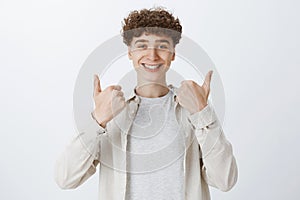 Waist-up shot of supportive and cheerful boyfriend with curly hair and sick eyebrows smiling satisfied as showing thumbs