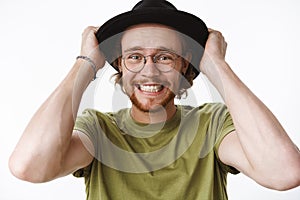 Waist-up shot of worried and anxious freaked out overwhelmed young bearded man with pierced nose holding hands on hat