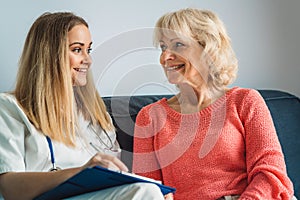 Waist up smiling senior woman sitting on the couch with her nurse