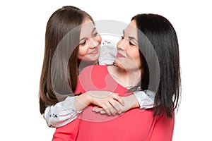 Waist up studio portrait of cute and playful schoolgirl embracing her mother. Happy family smiling background.