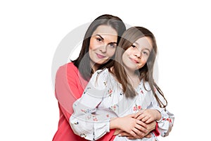Waist up studio portrait of cute and playful schoolgirl embracing her mother. Happy smiling family background.