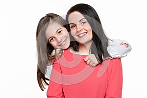 Waist up studio portrait of cute and playful schoolgirl embracing her mother. Happy smiling family background.