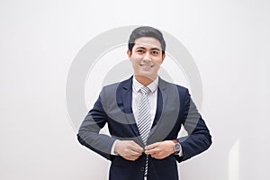 Waistup portrait of young smiling handsome businessman putting on suit jacket looking aside isolated on white