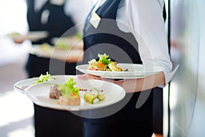 Waiter carrying plates with meat dish on some festive event