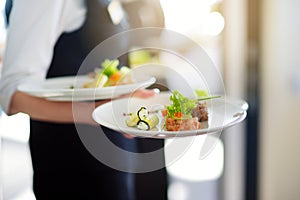 Waiter carrying plates with meat dish on some festive event