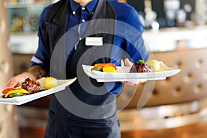 Waiter carrying plates with meat dish on some festive event