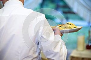 Waiter carrying plates with meat dish on some festive event, par