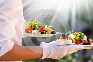 Waiter, carrying three plates with a rich salad at syny day