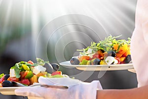 Waiter, carrying three plates with a rich salad at syny day