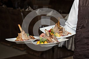 Waiter carrying tree plates with meat dish on some festive event